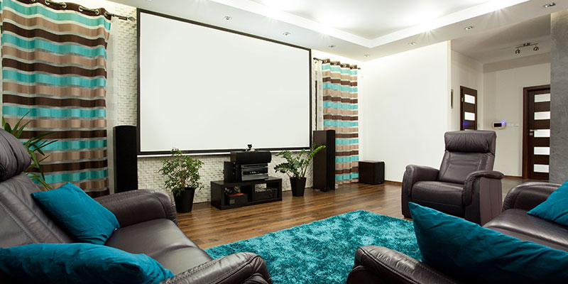 Contemporary home theater with a large projection screen, leather recliners, floorstanding speakers, striped curtains, and teal rug and pillows.